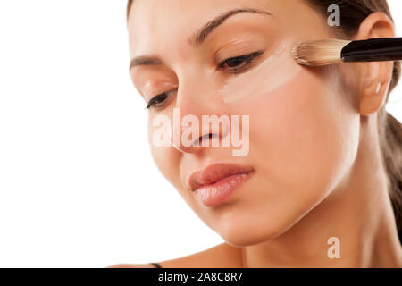 Una giovane donna applicato il correttore liquido sotto gli occhi con una spazzola Foto Stock