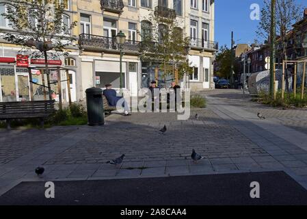 Tre uomini anziani sedersi a chiacchierare sulle panchine nel sole autunnale a Place Saint Antoine, Bruxelles, Belgio Foto Stock