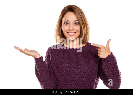 Giovane bella donna in un maglione viola e jeans, azienda oggetto immaginario sul palm Foto Stock