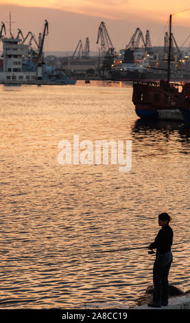 Varna, Bulgaria - 16 Luglio 2014: Donna pescatore sorge su una scogliera in Varna port al tramonto. Foto verticale Foto Stock