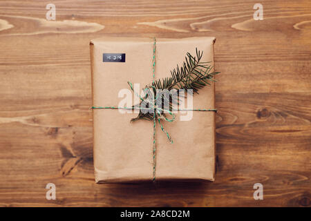 Close-up di scatola regalo confezionamento in carta da imballaggio marrone e decorate ramo fir giacente sul tavolo di legno Foto Stock