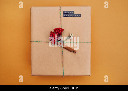 Regalo di natale Scatola decorata con bacche rosse e cannella isolato su sfondo giallo Foto Stock