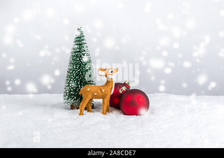 Renne in miniatura in piedi vicino a abete rosso e ornamenti Natale sotto la neve. Vacanze di Natale tema contro luce sfondo festosa wit Foto Stock