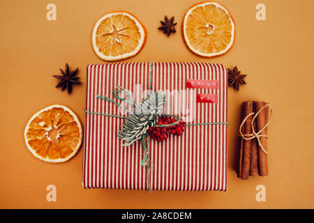 Close-up di regalo di Natale decorato con ramo di abete e bacche rosse con secchi arancio e cannella intorno isolato su sfondo arancione Foto Stock