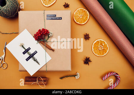 Close-up di cartolina fatti a mano che giace sul Natale decorati confezione regalo isolato su sfondo arancione Foto Stock
