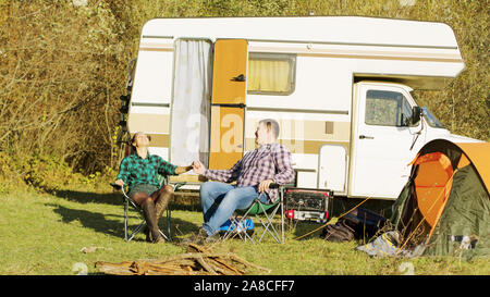 Rilassata giovane impostazione loro camping sedie davanti alla loro retrò camper. Tenda da campeggio. Foto Stock