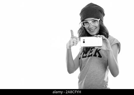 Studio shot di felice geek girl sorridere mentre di scattare una foto con il cellulare e dando pollice in alto Foto Stock