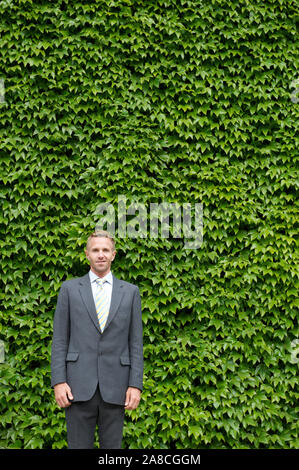Ritratto di imprenditore all'aperto in piedi di fronte a un muro di Bright Green ivy spazio copia Foto Stock