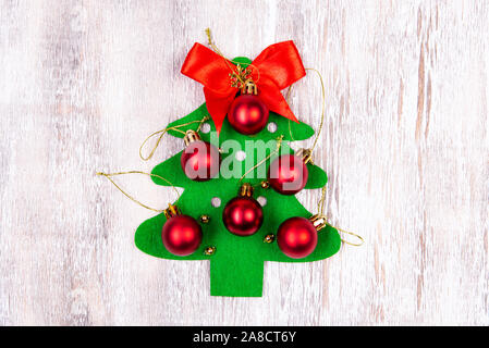 Su una tavola di legno si trova un feltro albero di Natale fatto da mani con palline rosse e un fiocco rosso nella parte superiore. Artigianato di natale Foto Stock