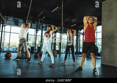 Un gruppo di atleti muscolare facendo allenamento in palestra. Ginnastica, formazione fitness flessibilità. Attivo e uno stile di vita sano, gioventù, bodybuilding. Formazione in affondi e esercizi di stretching. Foto Stock