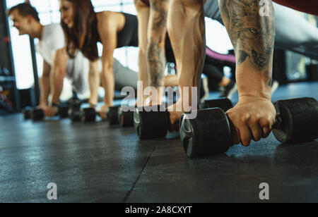 Un gruppo di atleti muscolare facendo allenamento in palestra. Ginnastica, formazione fitness flessibilità. Attivo e uno stile di vita sano, gioventù, bodybuilding. Stretta di mano con pesi di formazione. Foto Stock