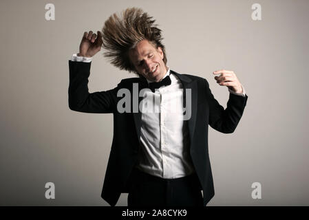 Giovane uomo in pieno tuxedo ballando con lunghi capelli biondi battenti Foto Stock