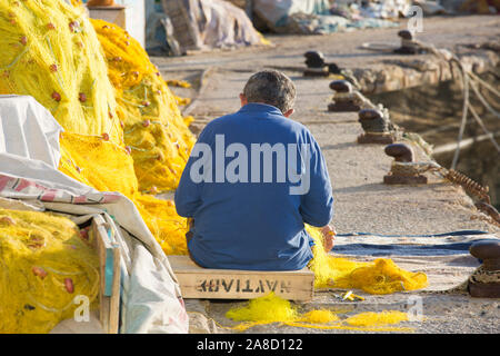 Heraklion, Creta, Grecia. Pescatore che mentendo rete colorata accanto al porto veneziano, vista posteriore. Foto Stock