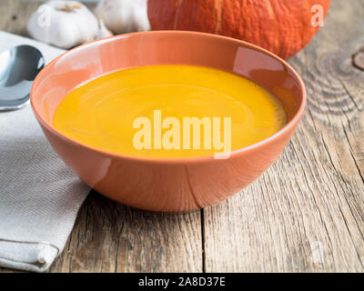 Zuppa di zucca in marrone piastra e zucca, aglio, igienico, cucchiaio su un età compresa tra lo sfondo di legno Foto Stock