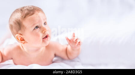 Ritratto di carino toddler boy giacente sul letto. Neonato in camera da letto. Baby giace sulla sua pancia e solleva la testa. Foto Stock