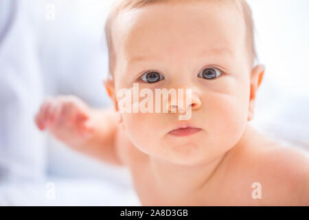 Ritratto di carino toddler boy giacente sul letto. Neonato in camera da letto. Baby giace sulla sua pancia e solleva la testa. Foto Stock