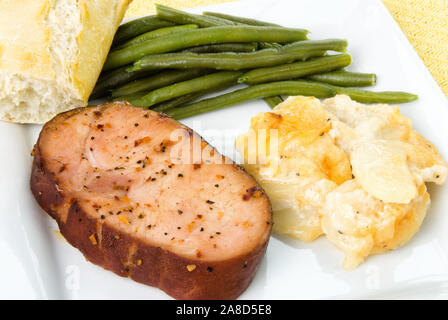 Affumicato di maiale disossate chop holiday pasto servito con fagiolini e smerlata gratinati patate e una baguette cotta rotolo. Girato in luce naturale. Foto Stock