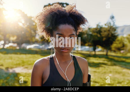 Ritratto di uno sportivo americano africano giovane donna con gli auricolari nelle orecchie la sua ascoltando musica guardando la fotocamera - determinata fitness donna nera in Foto Stock