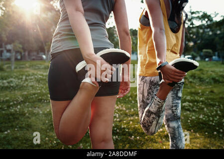 Close-up di due giovani femmine allungando le gambe - due donna sportiva stretching loro quads prima dell'esecuzione Foto Stock