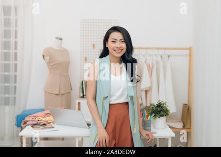 Giovani asiatici designer di moda sorridente e in piedi davanti al banco in officina Foto Stock