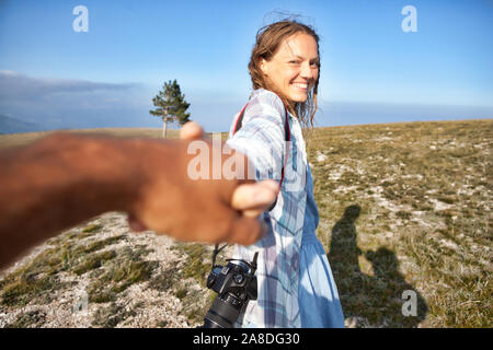 Un escursionista sorridente ragazza con zaino su una scogliera. Mano amica di aiutare. Un partner aiuta una ragazza a scalare una montagna. Il lavoro di squadra. Foto Stock