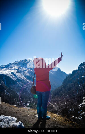 Una donna in abiti invernali permanente sulla cima della roccia di un nevato Rocky Mountain. Vista posteriore. Neve profonda e Blizzard tutto intorno. Volto umano al fac Foto Stock