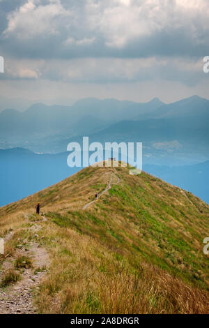 Sentiero con lungo il crinale della montagna con una panca in legno alla fine con viste panoramiche sulla valle e le gamme della montagna nella distanza. Foto Stock