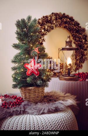 Piccolo portatile il piano portapaziente albero di Natale decorato sul tavolo, partito spie illuminate, feltro rosso ornamento del tessuto. Lampadina della luce di lanterna con cono di pino wreat Foto Stock