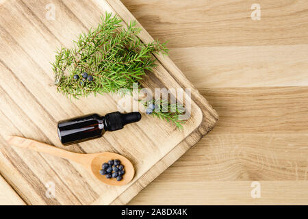 Piatto vista Lay Juniper latin Juniperus communis olio essenziale di bacca in bottiglia marrone contagocce, ramificazione di albero di ginepro con coni di fiducia e frutti di bosco sparso Foto Stock