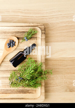 Piatto vista Lay Juniper latin Juniperus communis olio essenziale di bacca in bottiglia marrone contagocce, ramificazione di albero di ginepro con coni di fiducia e frutti di bosco sparso Foto Stock