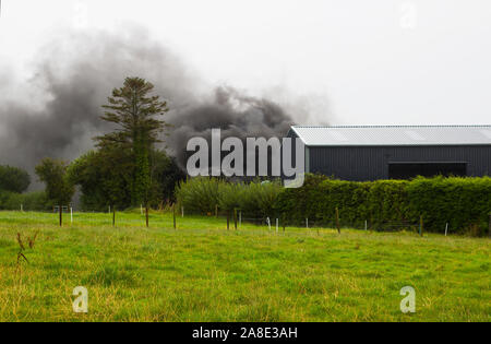 21 agosto 2019 denso fumo nero dalla combustione di pneumatici in gomma in modo irresponsabile riempiendo il cielo su una fattoria in County Fermanagh in Irlanda del Nord Foto Stock