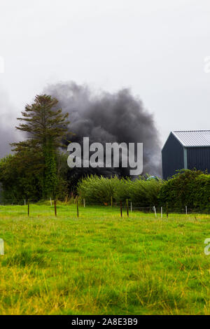 21 agosto 2019 denso fumo nero dalla combustione di pneumatici in gomma in modo irresponsabile riempiendo il cielo su una fattoria in County Fermanagh in Irlanda del Nord Foto Stock