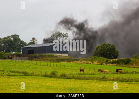 21 agosto 2019 denso fumo nero dalla combustione di pneumatici in gomma in modo irresponsabile riempiendo il cielo su una fattoria in County Fermanagh in Irlanda del Nord Foto Stock