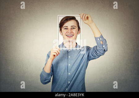 Ragazzo adolescente che ricopre la faccia utilizzando un foglio di carta per la stampa fotografica con autoritratto schizzo, come una maschera per nascondere la vera emozione. Vita privata, dissembler falso Foto Stock