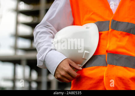 Lavoratore con bianco casco di sicurezza e giubbotto di colore arancione. Costruzione e sito industriale concetto dei lavoratori Foto Stock