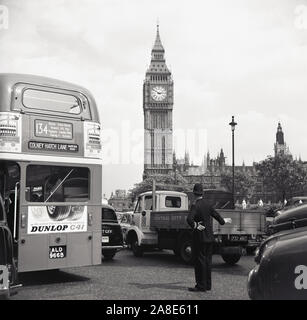 Anni sessanta, storici British poliziotto che dirige il traffico a Piazza del Parlamento, Londra, Inghilterra, con la torre dell orologio visibile in lontananza. Un 134 autobus Routemaster andando a prendere per Colney Hatch Lane può essere visto come pure altre automobili e camion dell'epoca. Foto Stock