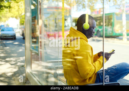 African giovane uomo Ascoltare musica presso la fermata degli autobus Foto Stock