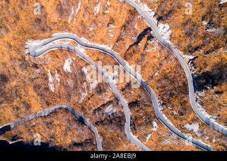 Vista aerea di montagna tortuosa strada in autunno o in inverno. Paesaggio con il giallo dei prati di erba secca e stretta strada asfaltata. Vista dall'alto. Foto Stock