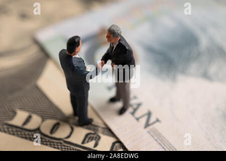 La figura imprenditore in piedi sul dollaro e yuan banconota, tenendo le mani per il successo in accordi commerciali. Concetto di guerra di trading Foto Stock