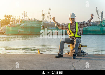 Ingegneri che indossa un casco di sicurezza e seduta. Egli è il sollevamento di due mani e si sente felice per il raggiungimento del successo. Concetto del concetto di determinazione di un Foto Stock