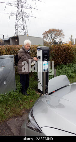 Donna collegando in EV Nissan Leaf al veicolo elettrico stazione di carica; NEC Est Car Park, Birmingham Foto Stock