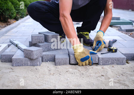 Il master in Guanti gialli getta pietre per pavimentazione in strati. Giardino percorso di mattoni da pavimentazione lastricatore professionale lavoratore. La posa di cemento grigio Pavimentazioni Foto Stock