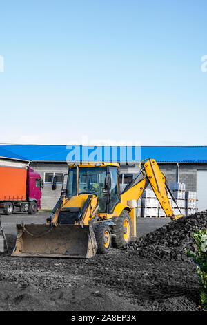 Il giallo tutte le ruote motrici del caricatore retroescavatore sorge sul cantiere pronto per workind sul sito in costruzione. Foto Stock