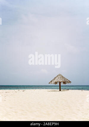 Un palm frond ombrello appoggiato sull'isola isolata spiaggia di Mopion in Saint Vincent e Grenadine. Foto Stock