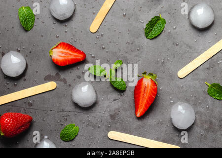 Fragole e foglie di menta vicino a cubetti di ghiaccio e gelato bastoni. Gelato il concetto di sfondo. Foto Stock