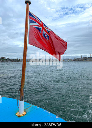 Red Ensign battenti nella brezza del mare con Southampton Docks in background. Foto Stock