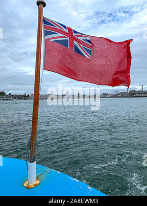 Red Ensign battenti nella brezza del mare con Southampton Docks in background. Foto Stock