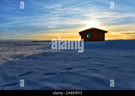 Cabina isolata circondata da neve profonda nella remota area di Hvoll nel sud dell'Islanda al tramonto Foto Stock