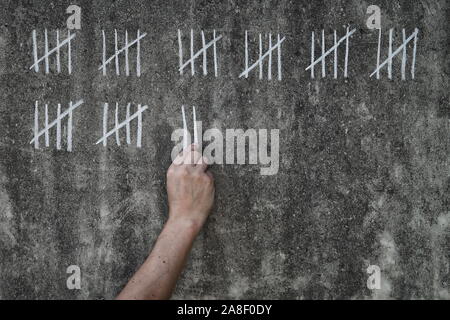 Conteggio dei giorni in prigione - prigioniero maschio scrivere righe bianche di gesso su una sporca parete in calcestruzzo Foto Stock