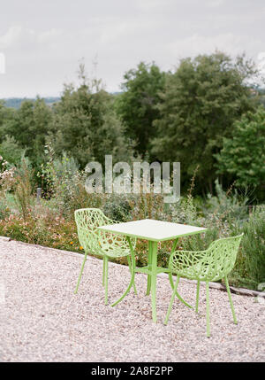 Contemporanea verde pastello giardino con sedie e tavolo poggiare su una superficie di ghiaia le piante in una collina vicino giardino Toscana, Italia. Foto Stock